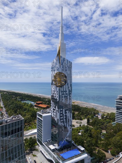 Futuristic skyscraper with clock on the coast, surrounded by trees and sea under blue sky, aerial view, Batumi Tower with Ferris wheel, Batumi, Black Sea, Adjara region, Adjara, autonomous republic, Georgia