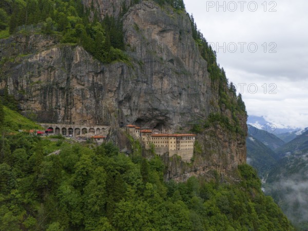 A monastery embedded in a steep rock face surrounded by lush forests and mountains under an overcast sky, aerial view, Sumela Monastery, Sümela Manastiri, Maçka, Macka, Trabzon Province, Turkey