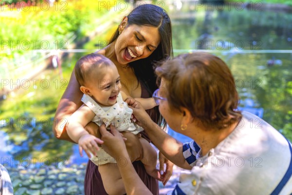 Happy latin family enjoying a sunny day in a park, mother holding her baby while grandmother is playing with her