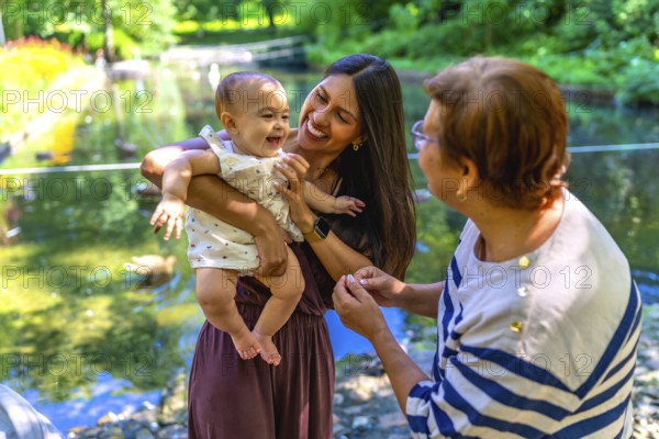 Grandmother, mother and granddaughter spending time together in a park, enjoying the summer and having fun by the pond