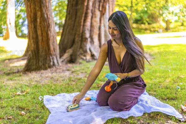 Latin mom arranging colorful baby toys on blanket in park, enjoying quality time with her child in nature