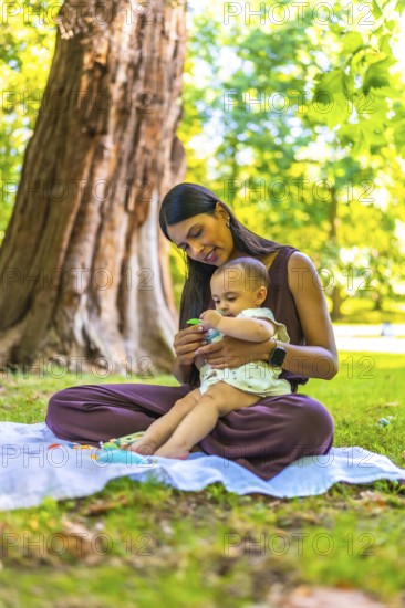 Latin mother and daughter spending time together in a park, playing with toys on a blanket under a tree