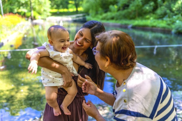 Latin family, including a grandmother, mother, and baby daughter, are enjoying quality time together in a park setting, creating cherished memories