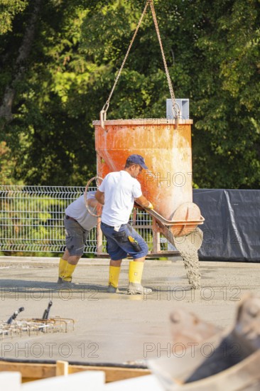 Two construction workers pouring concrete from a concrete mixer on a building site, surrounded by trees, car park construction, Calw, Germany