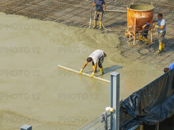 Workers smoothing concrete on a construction site while a concrete mixer stands in the background, car park construction, Calw, Germany