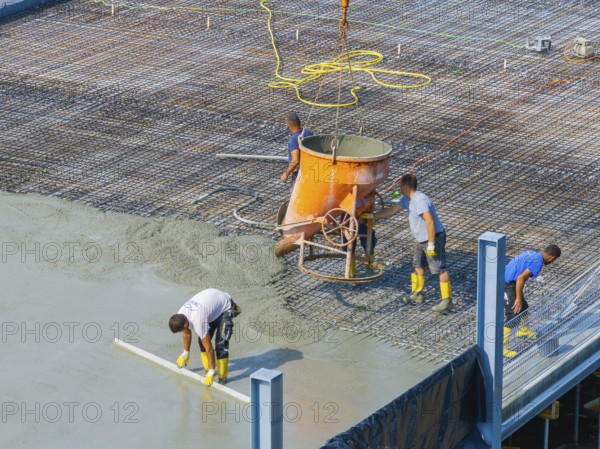 Workers pouring concrete on a construction site with concrete mixer and steel frame structure in the background, car park construction, Calw, Germany