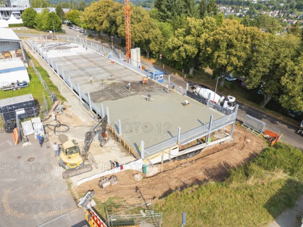 Construction site with concreted area, machines and construction workers, surrounded by green trees, car park construction, Calw, Germany