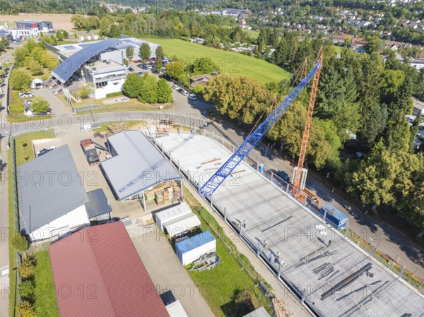 Construction site under blue sky with crane in urban environment and many trees, car park construction, Calw, Germany