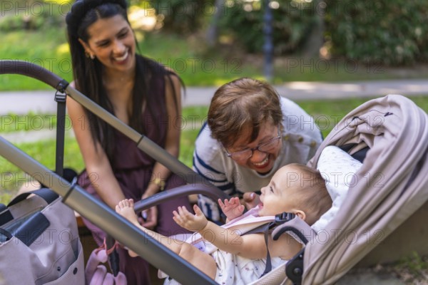 Grandmother and mother taking care of a baby girl in a stroller, playing and laughing together in a park