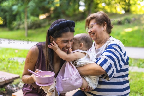Latin family enjoying time together in park, grandmother holding granddaughter while mother is preparing a meal