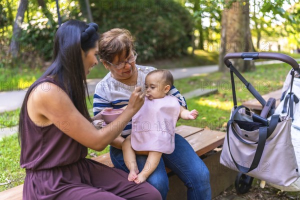 Latin family enjoying a sunny day outdoors, with grandmother and mother lovingly feeding a baby girl while sharing smiles and laughter
