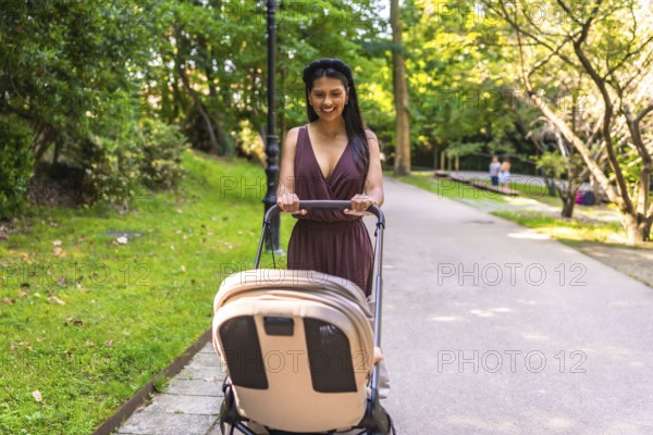 Latin mother pushing a stroller with a happy baby inside, enjoying a sunny day while walking through a peaceful park filled with greenery