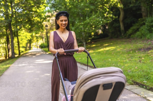 Latin mother enjoying a walk in the park, pushing a stroller with her baby inside, on a sunny day