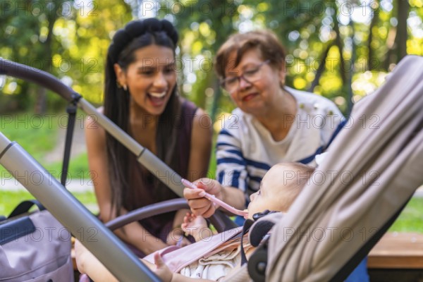 Grandmother feeds baby girl sitting in stroller, while mother watches, enjoying family time together in park