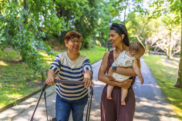Grandmother, mother, and baby girl enjoying a sunny day at the park, pushing a stroller and spending quality time together