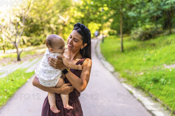 Latin mother holding her baby daughter, smiling and enjoying a walk in a park during a sunny day