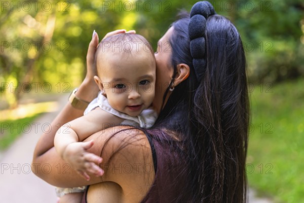 Mother cuddling her baby girl while strolling through a park, savoring a sunny day filled with family love and joyful bonding