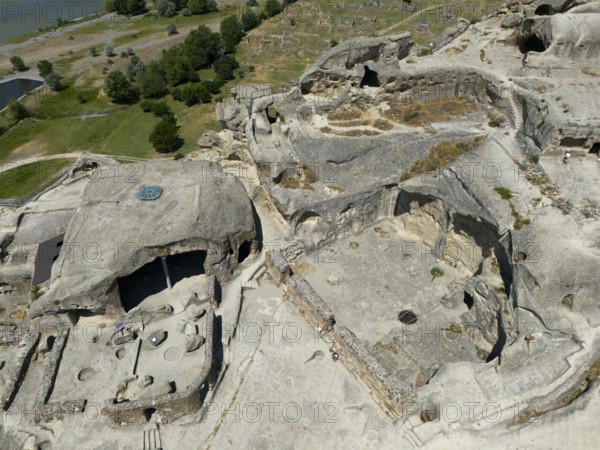Cave complex with ruins near a river, surrounded by lush nature and rocks, aerial view, cave town Uplistsikhe, Uplistsikhe, river Kura or Mtkvari, Inner Kartlia region, Shida Kartli, Georgia
