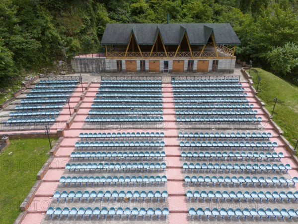 An amphitheatre with many rows of seats and a covered stage against a wooded backdrop, aerial view, Green Theatre, Tsageri, Racha-Lechkhumi region and Lower Svaneti, Georgia