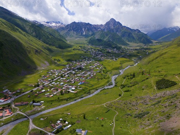 Wide valley with river and village, surrounded by mountains under a partly cloudy sky, aerial view, view into the valley of the river Terek, Toti, Kazbegi, Qasbegi, Stepantsminda, Georgian Military Road, Mtskheta-Mtianeti Province, High Caucasus, Georgia