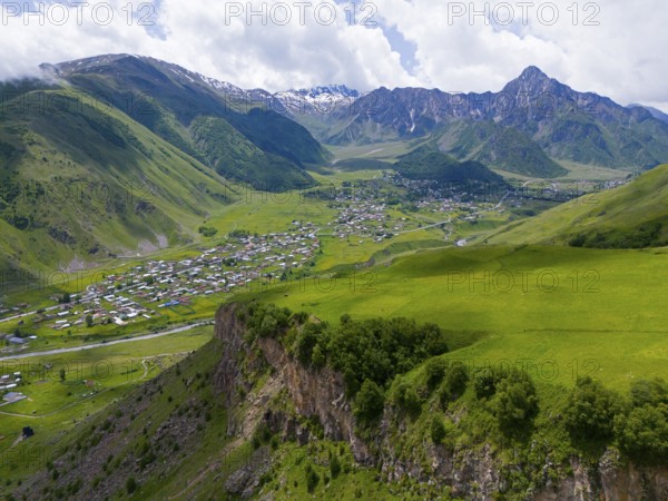 Lush valley with small village and rock face, framed by forested mountains under clouds, aerial view, view into the valley of the river Terek, Toti, Kazbegi, Qasbegi, Stepantsminda, Georgian Military Road, Mtskheta-Mtianeti Province, High Caucasus, Georgia
