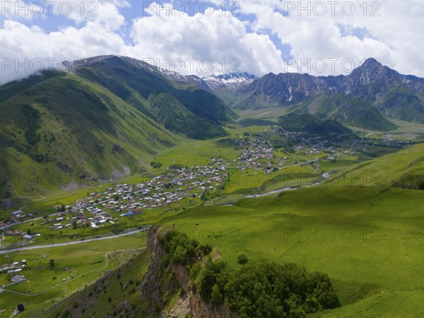 Panoramic view of green valley with village and mountains under a cloudy sky, aerial view, view into the valley of the river Terek, Toti, Kazbegi, Qasbegi, Stepantsminda, Georgian Military Road, Mtskheta-Mtianeti Province, High Caucasus, Georgia