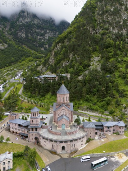 Majestic red brick church in a picturesque mountain landscape under cloudy atmosphere, aerial view, Dariali monastery complex, located in the Dariali gorge of the Tergi river, Terek, Khevi mountain region, Georgian Military Road, Mtskheta-Mtianeti province, High Caucasus, Georgia