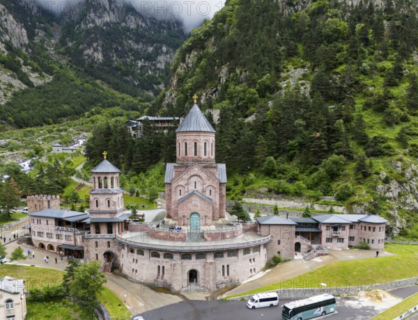 Impressive red brick church surrounded by forested mountains under a cloudy sky, aerial view, Dariali Monastery Complex, located in the Dariali Gorge of the Tergi River, Terek, Khevi Mountain Region, Georgian Military Road, Mtskheta-Mtianeti Province, High Caucasus, Georgia