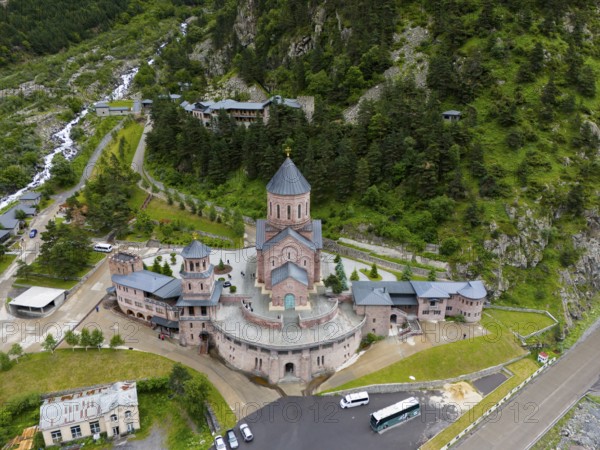 Red brick church in a picturesque mountain landscape, surrounded by forests and clouds in the sky, aerial view, Dariali monastery complex, located in the Dariali gorge of the Tergi river, Terek, Khevi mountain region, Georgian Military Road, Mtskheta-Mtianeti province, High Caucasus, Georgia