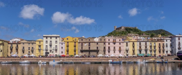 Sardinia, panoramic photo with houses and promenade on the river Temo, guests at the restaurants and parasols, blue sky with clouds, Castello Malaspina, Castello di Serravalle, Bosa, Europe, province of Oristano, Italy, old town, architecture, atmosphere, Castello Malaspina, recreation, dining area, river Temo, riverside, leisure, guests, culture, landscape, panoramic photo, promenade, travelling, restaurants, castle, sights, sightseeing, summer, parasols, city view, city life, tourism, tourist, tourist destination, urban, residential buildings, clouds, blue sky, European, historic buildings, picturesque, Mediterranean