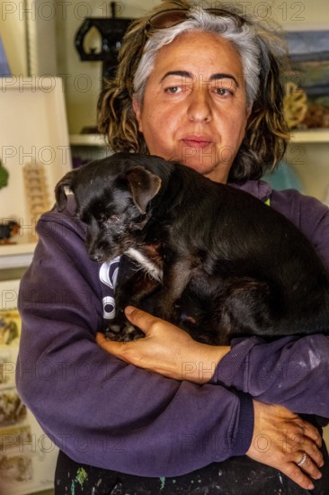 Sardinia, Pina Monne, portrait of woman and dog on arm, artist, Tinnura, Europe, Oristano province, Italy, arm, expression, gaze, detail, woman, middle-aged woman, portrait of woman, face, pet, dog, interior, interaction, small town, context, culture, artwork, painting, human, facial expression, portrait, pose, region, sight, sightseeing, style, animal, animal husbandry, animal love, tourism, tradition, environment, European, artistic, local, Mediterranean, female