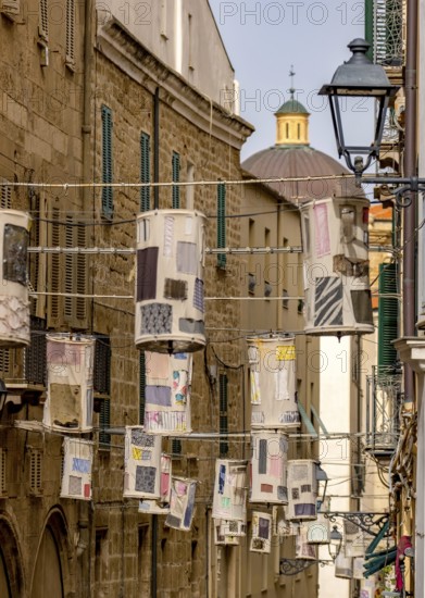 Sardinia, lanterns made of fabric remnants patchwork on power lines between the houses above the alleyway, old town, Alghero, Europe, province of Sassari, Italy, evening, architecture, atmosphere, lighting, design, photo scene, alleys, sky, houses, culture, arts and crafts, lanterns, patchwork, perspective, retro-chic, romance, shadow, sightseeing, summer, summer evening, city, fabric remnants, alleyway, alleyway scene, power lines, tourism, urban, colourful, decoration, historic buildings, hanging, creative, Mediterranean, traditional, visual arts