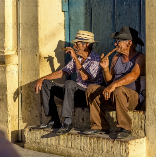 Two old Cubans smoking cigars and sitting on a staircase in the warm light of the sunset, Trinidad, Cuba, Sancti Spíritus, Sancti Spíritus