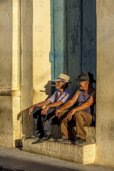 Two old Cubans smoking cigars and sitting on a staircase in the warm light of the sunset, Trinidad, Cuba, Sancti Spíritus, Sancti Spíritus