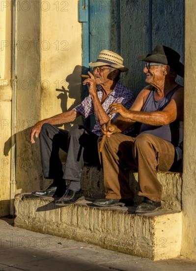 Two old Cubans smoking cigars and sitting on a staircase in the warm light of the sunset, Trinidad, Cuba, Sancti Spíritus, Sancti Spíritus