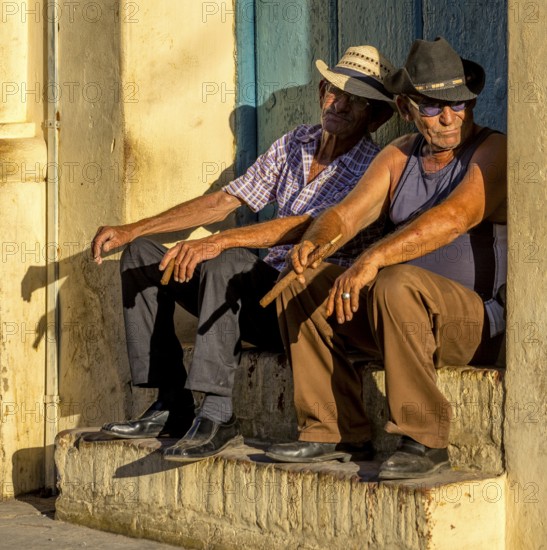 Two old Cubans smoking cigars and sitting on a staircase in the warm light of the sunset, Trinidad, Cuba, Sancti Spíritus, Sancti Spíritus