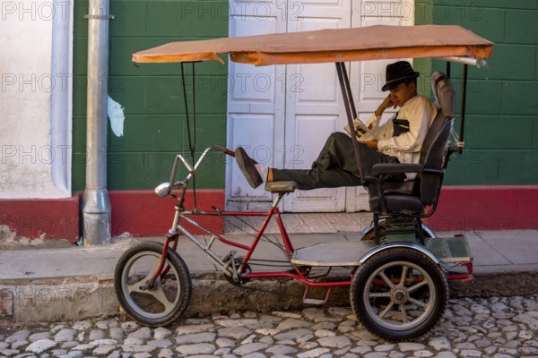 Rickshaw driver waiting for customers and reading a novel, Trinidad, Cuba, Sancti Spíritus, Sancti Spíritus