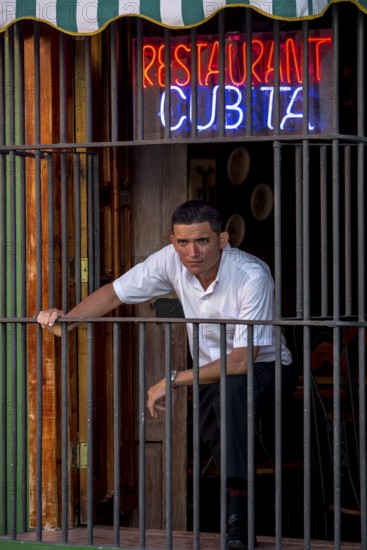 Waiter waiting for customers behind the window bars of the Cubita Restaurant, Trinidad, Cuba, Sancti Spíritus, Sancti Spíritus