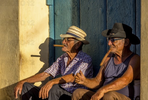 An old Cuban smokes a cigar and sits on a staircase in the warm light of the sunset, Trinidad, Cuba, Sancti Spíritus, Sancti Spíritus