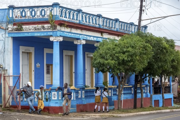Typical Cuban blue house with columns, workers and girls in school uniform, Viñales, Cuba, Pinar del Río, Viñales, Pinar del Río