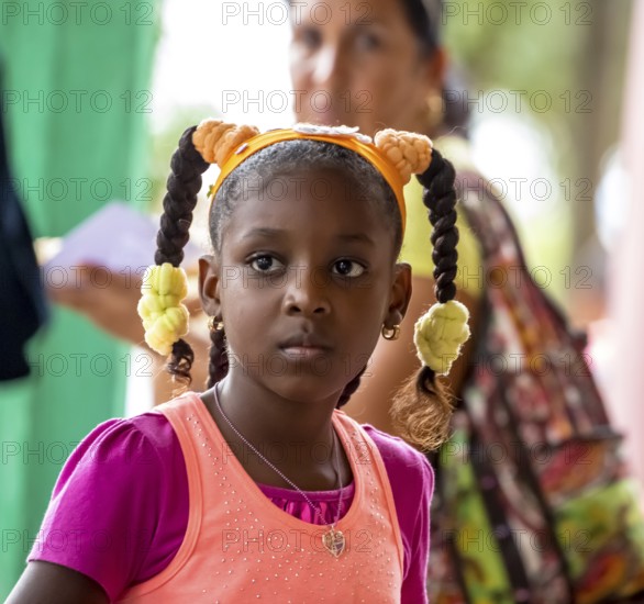 Young girl with pinned-up pigtails at a Cuban pizza stand with her family, Viñales, Cuba, Pinar del Río, Viñales, Pinar del Río