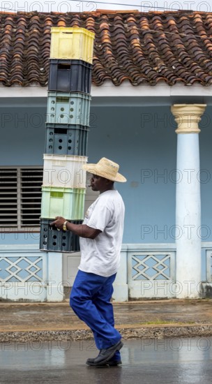 Cuban man with hat carrying and balancing crates of drinks across a street in Vinales, Viñales, Cuba, Pinar del Río, Viñales, Pinar del Río