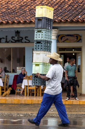 Cuban man with hat carrying and balancing crates of drinks across a street in Vinales, Viñales, Cuba, Pinar del Río, Viñales, Pinar del Río