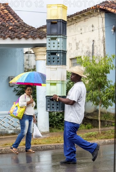 Cuban man with hat carrying and balancing crates of drinks across a street in Vinales, Viñales, Cuba, Pinar del Río, Viñales, Pinar del Río