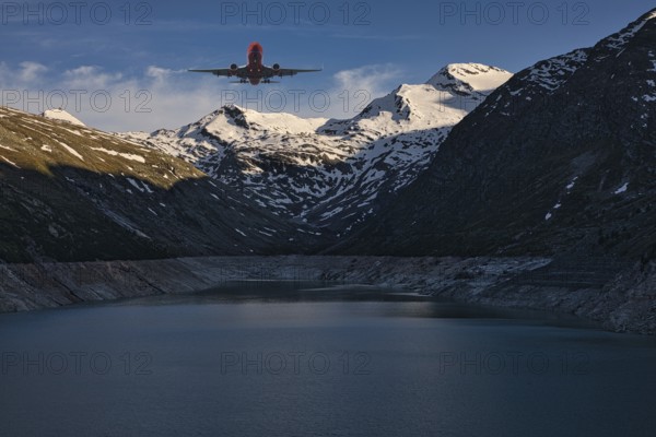 Aeroplane flying over a mountain lake with snow-covered peaks under a blue sky, Mattmark reservoir, Saas Almagell, Saas Grund, Canton Valais, Switzerland