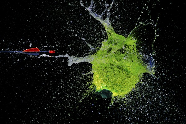A green water balloon bursts powerfully under the impact of an arrow, against a dark background, high-speed shot, water balloon, arrow