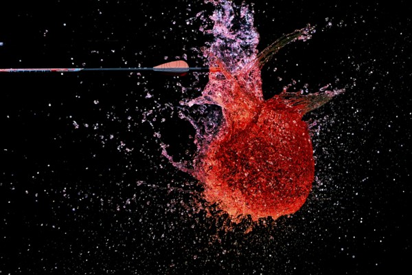 A red water balloon is penetrated by an arrow and creates a lively, powerful water scene, high-speed shot, water balloon, arrow