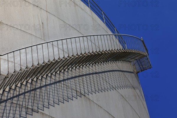 A metal staircase casts a shadow on a cylindrical industrial building under a clear blue sky, elevated tank, chemical, company, Grenzach- Wyhlen, Baden-Württemberg, Germany