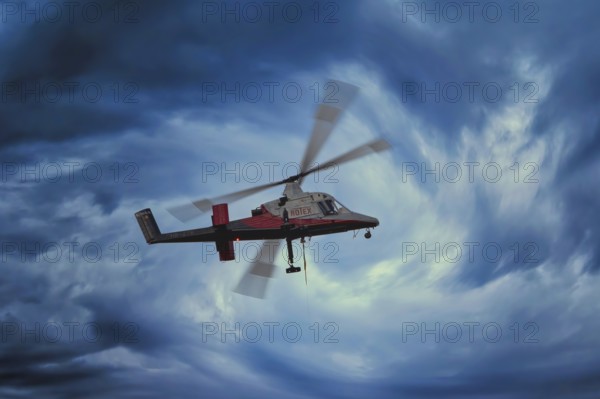 A helicopter flies through a dramatic, stormy blue sky, transport helicopter, timber transport, Saas Grund, Canton Valais, Switzerland