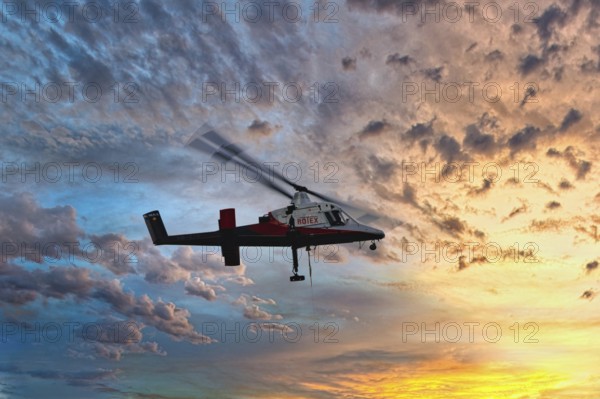 A helicopter flies in front of a colourful sunset with dramatic cloud formations, transport helicopter, timber transport, Saas Grund, Canton Valais, Switzerland